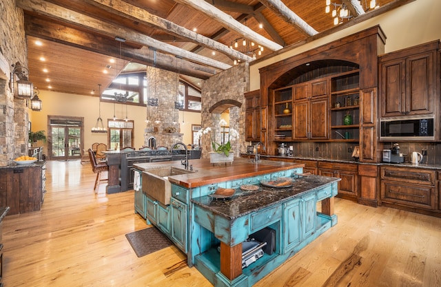 kitchen featuring black microwave, wood ceiling, dark stone counters, high vaulted ceiling, and a center island with sink