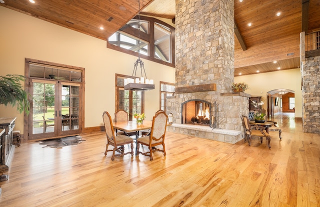 dining room with light wood-type flooring, high vaulted ceiling, and a stone fireplace