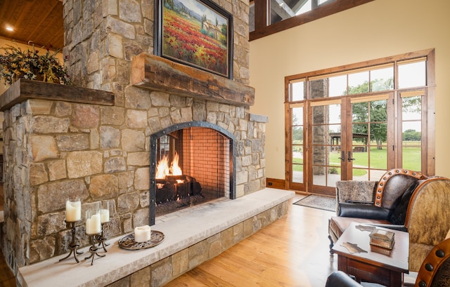 interior space with french doors, a stone fireplace, a high ceiling, and light hardwood / wood-style floors