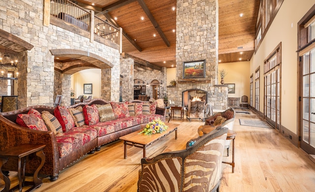 living room with wooden ceiling, light hardwood / wood-style floors, a stone fireplace, high vaulted ceiling, and beam ceiling