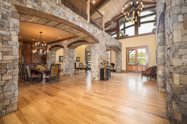 interior space featuring light wood-type flooring, high vaulted ceiling, a chandelier, and decorative columns