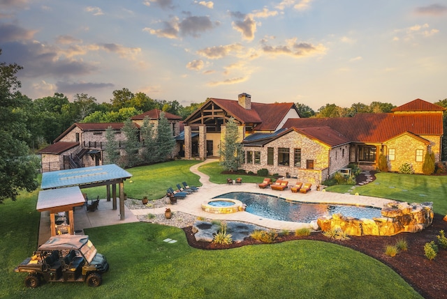 pool at dusk featuring an in ground hot tub, a lawn, and a patio