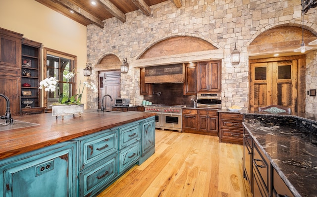 kitchen with light hardwood / wood-style flooring, custom range hood, beam ceiling, double oven range, and butcher block counters