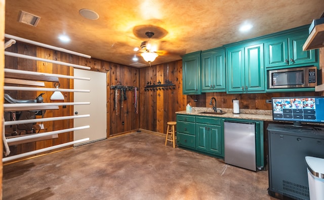 kitchen with light stone countertops, concrete flooring, appliances with stainless steel finishes, sink, and wooden walls