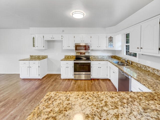 kitchen with appliances with stainless steel finishes, white cabinetry, sink, and light hardwood / wood-style floors