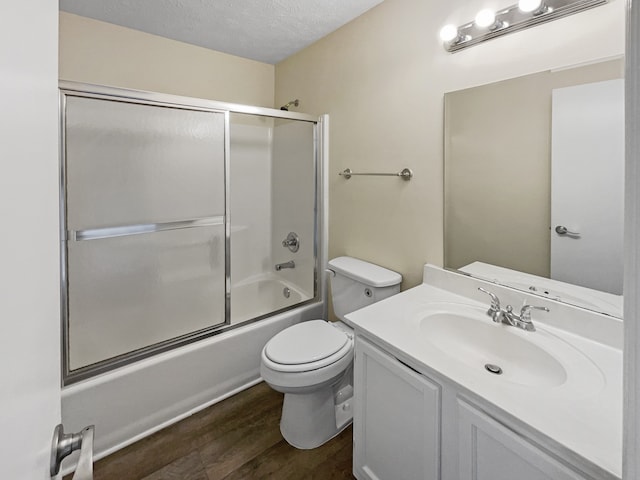 full bathroom featuring hardwood / wood-style flooring, toilet, vanity, bath / shower combo with glass door, and a textured ceiling