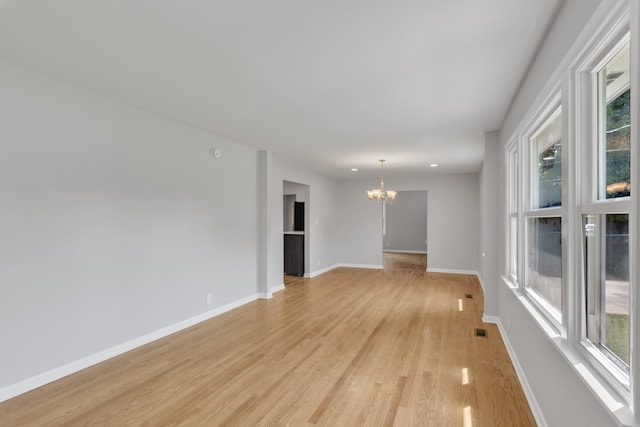 unfurnished room featuring a healthy amount of sunlight, an inviting chandelier, and light hardwood / wood-style flooring