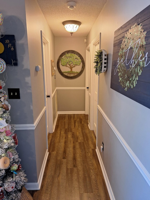 corridor with wood finished floors, baseboards, and a textured ceiling