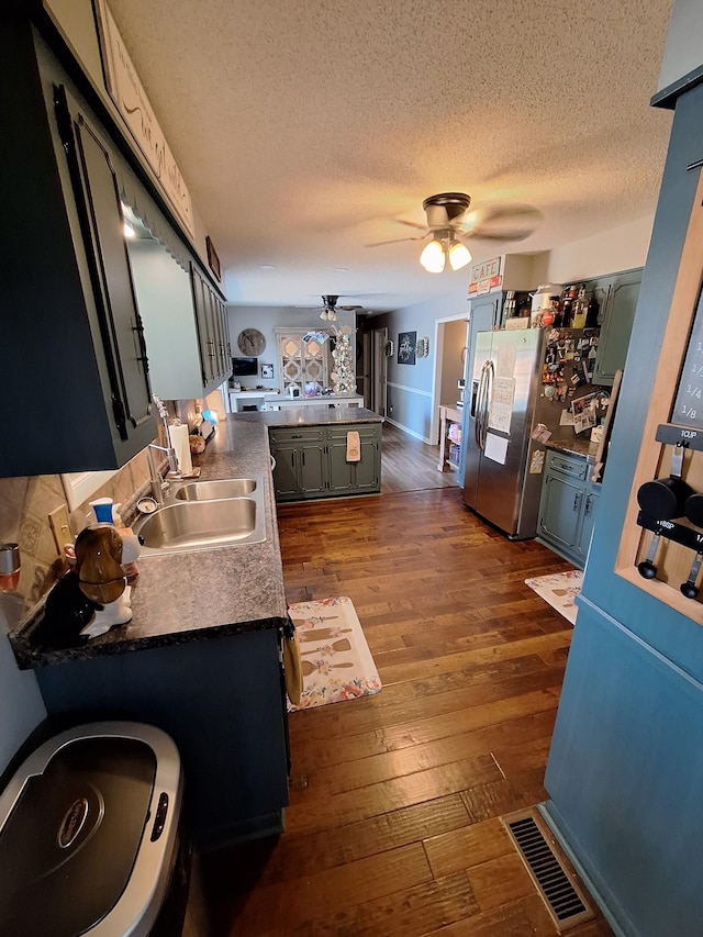 kitchen featuring visible vents, dark wood finished floors, stainless steel fridge, a ceiling fan, and a sink