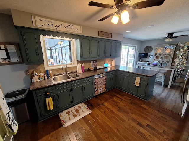 kitchen with dark countertops, dark wood-style flooring, a peninsula, and a sink