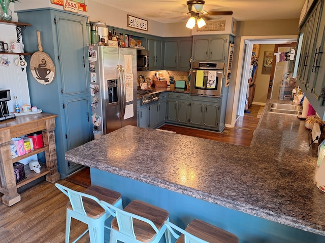 kitchen with dark wood-type flooring, kitchen peninsula, stainless steel appliances, and ceiling fan