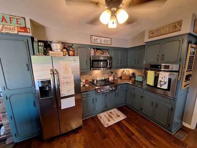 kitchen with dark countertops, a textured ceiling, dark wood finished floors, appliances with stainless steel finishes, and decorative backsplash