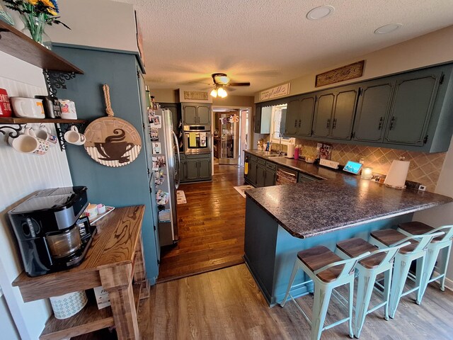 kitchen with a textured ceiling, stainless steel appliances, wood-type flooring, kitchen peninsula, and ceiling fan