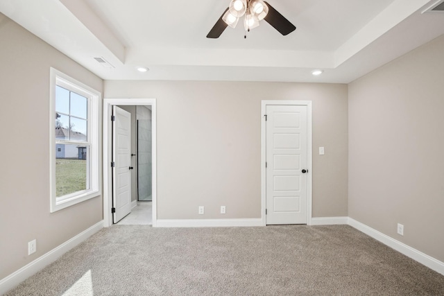 empty room with ceiling fan, light colored carpet, and a tray ceiling