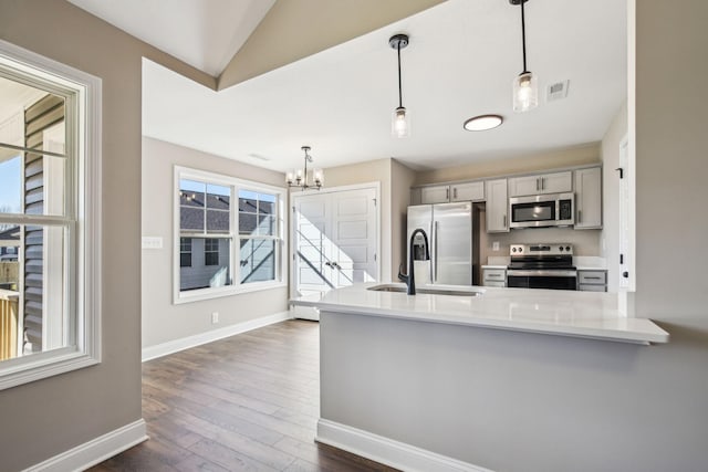 kitchen with pendant lighting, kitchen peninsula, sink, an inviting chandelier, and stainless steel appliances