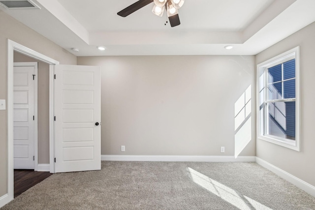 empty room featuring dark colored carpet, a tray ceiling, and ceiling fan