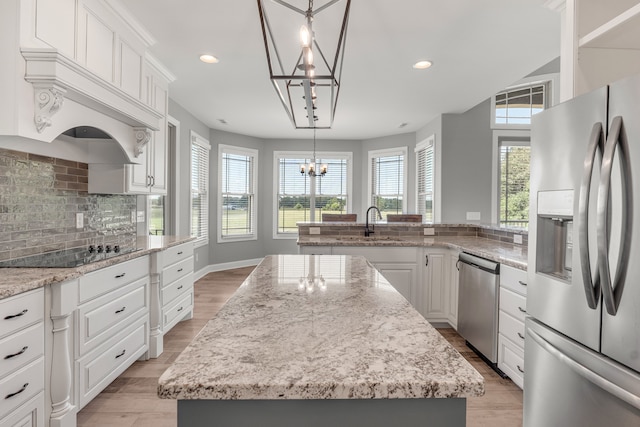 kitchen with a center island with sink, white cabinets, appliances with stainless steel finishes, and decorative light fixtures