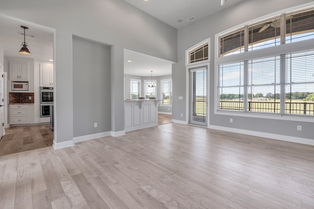 unfurnished living room with light wood-type flooring, a notable chandelier, and a towering ceiling