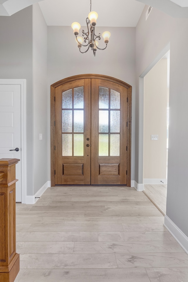 foyer entrance with french doors, a chandelier, and light hardwood / wood-style flooring