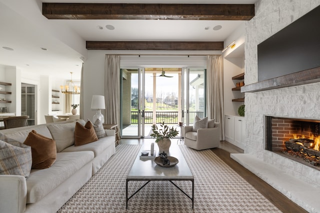 living room featuring beamed ceiling, hardwood / wood-style flooring, an inviting chandelier, and a stone fireplace