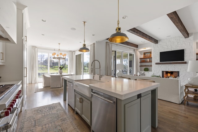 kitchen featuring dark hardwood / wood-style floors, a stone fireplace, an island with sink, stainless steel appliances, and a chandelier