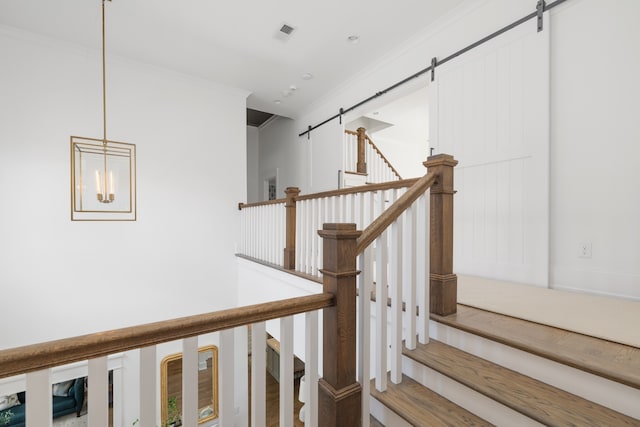 staircase with ornamental molding, wood-type flooring, a chandelier, and a barn door