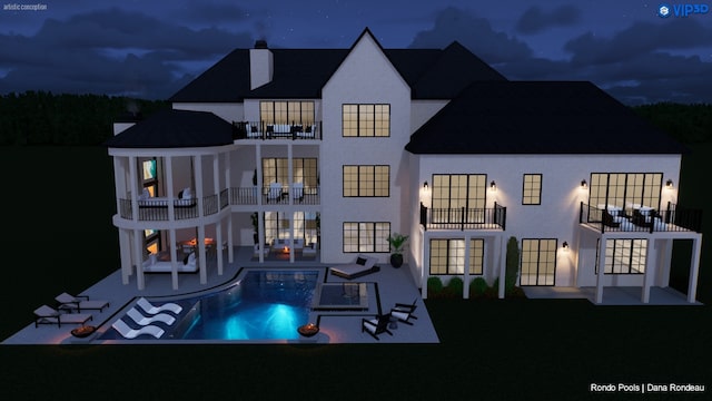 back house at night featuring a balcony, a patio area, and a fenced in pool