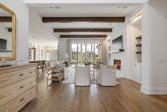 living room with an inviting chandelier, a fireplace, dark hardwood / wood-style floors, and beam ceiling