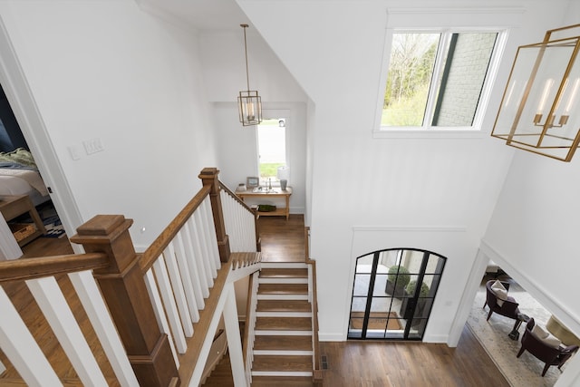 stairway featuring a towering ceiling, a healthy amount of sunlight, and hardwood / wood-style floors