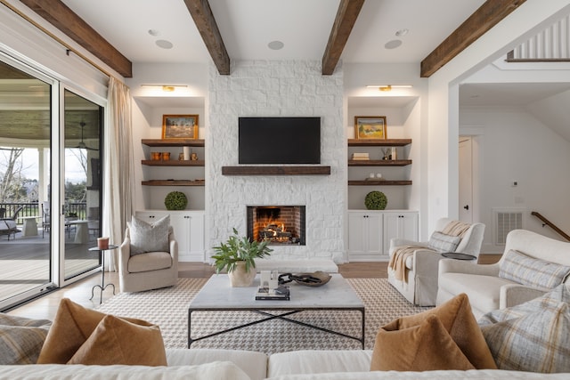 living room with built in shelves, beam ceiling, light hardwood / wood-style floors, and a stone fireplace