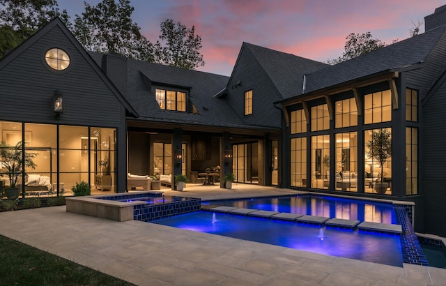 pool at dusk with a patio, an in ground hot tub, and pool water feature