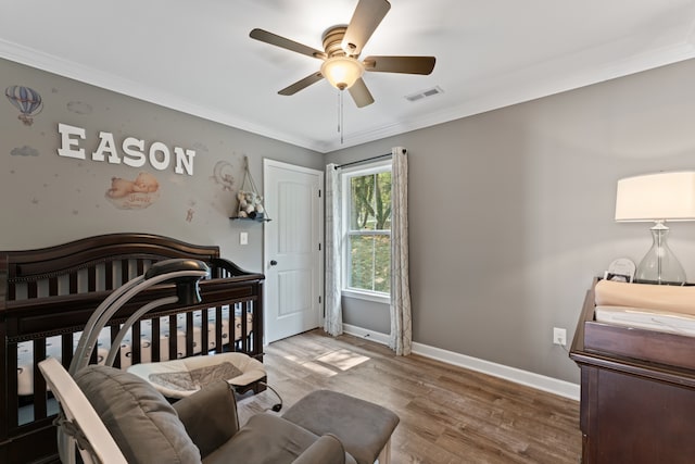 bedroom with ceiling fan, hardwood / wood-style flooring, a nursery area, and ornamental molding