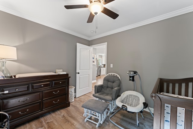 bedroom with ceiling fan, light hardwood / wood-style floors, crown molding, and a crib