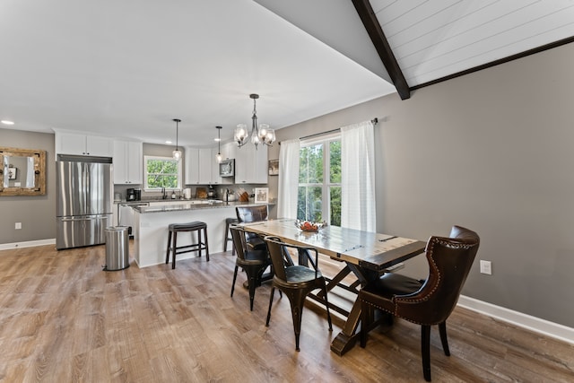 dining room with light hardwood / wood-style floors, a notable chandelier, and vaulted ceiling with beams