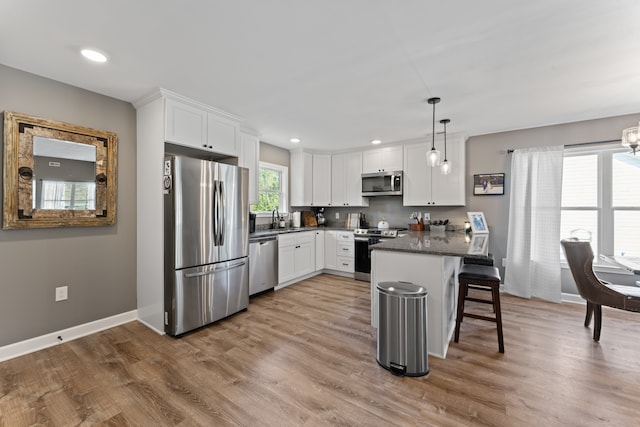 kitchen featuring hanging light fixtures, white cabinetry, a breakfast bar, appliances with stainless steel finishes, and hardwood / wood-style flooring