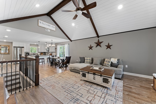 living room featuring ceiling fan with notable chandelier, light wood-type flooring, beamed ceiling, and high vaulted ceiling