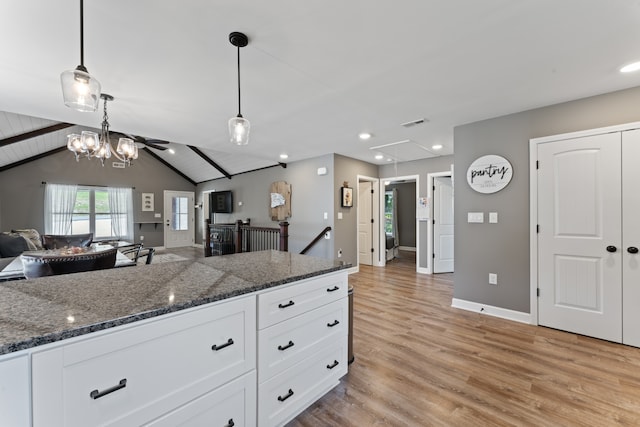 kitchen featuring pendant lighting, light hardwood / wood-style flooring, white cabinetry, lofted ceiling with beams, and dark stone counters