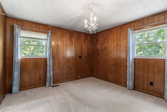 unfurnished room with wooden walls, an inviting chandelier, and light carpet