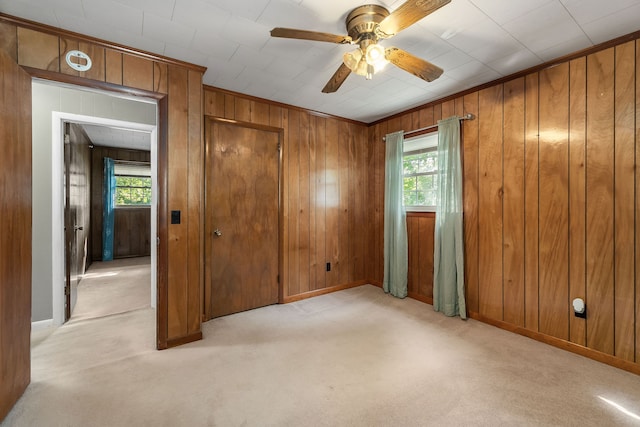 unfurnished room featuring light colored carpet, a wealth of natural light, wood walls, and ceiling fan