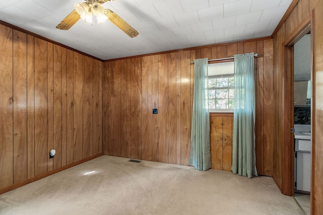 carpeted empty room featuring ceiling fan, wooden walls, and crown molding