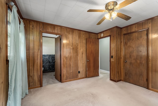 unfurnished bedroom featuring wood walls, ceiling fan, light colored carpet, and ensuite bathroom