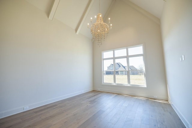 empty room with beamed ceiling, high vaulted ceiling, a notable chandelier, wood finished floors, and baseboards