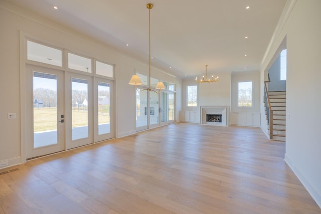 unfurnished living room with light wood-type flooring, visible vents, a fireplace, crown molding, and stairs