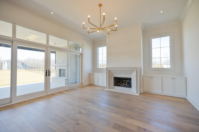 unfurnished living room with baseboards, light wood finished floors, an inviting chandelier, a fireplace with flush hearth, and ornamental molding