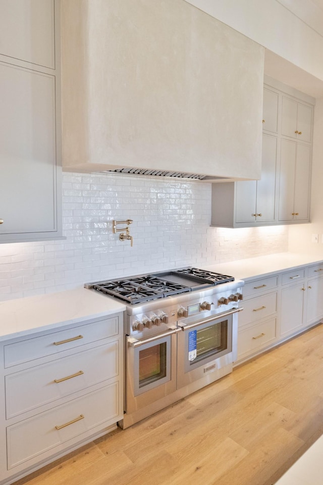 kitchen featuring backsplash, double oven range, light countertops, light wood-style flooring, and white cabinets