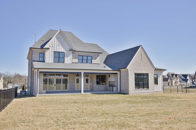 rear view of house with brick siding, board and batten siding, a yard, a fenced backyard, and a patio area