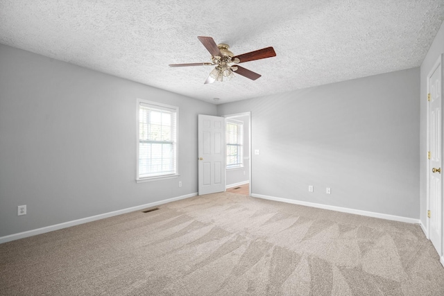 unfurnished room with ceiling fan, a textured ceiling, visible vents, carpet floors, and baseboards
