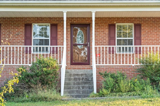 entrance to property with a porch and brick siding