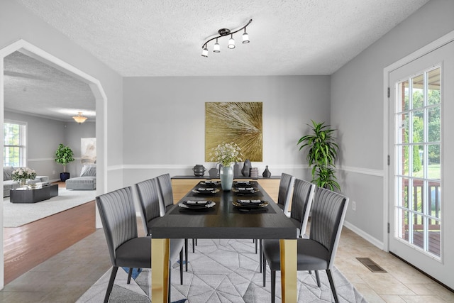 dining room with arched walkways, stone finish floor, a textured ceiling, and visible vents