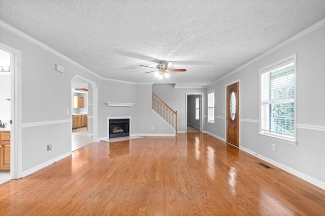 unfurnished living room featuring ceiling fan, light wood-style floors, a textured ceiling, stairs, and a fireplace with flush hearth